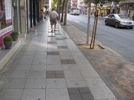 Trottoir /
                    B�rgersteig in weissen Platten mit schwarzen
                    Tupfern, und Baumbereiche in gelb-rot-schwarzen
                    Gartensteinen