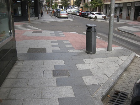 Trottoir / B�rgersteig in weissen
                        Platten mit schwarzen B�ndern und Zahnradband
                        bei einer Kreuzung