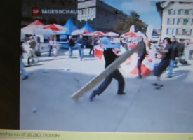 6.10.2007: Schande von Bern 011,
                        Bundesplatz 02: Der Vermummte wirft die Bank
                        gegen Passanten