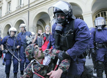 6.10.2007: Schande von Bern 020: Polizist
                        mit Gasmaske gegen Clown in Armeeuniform