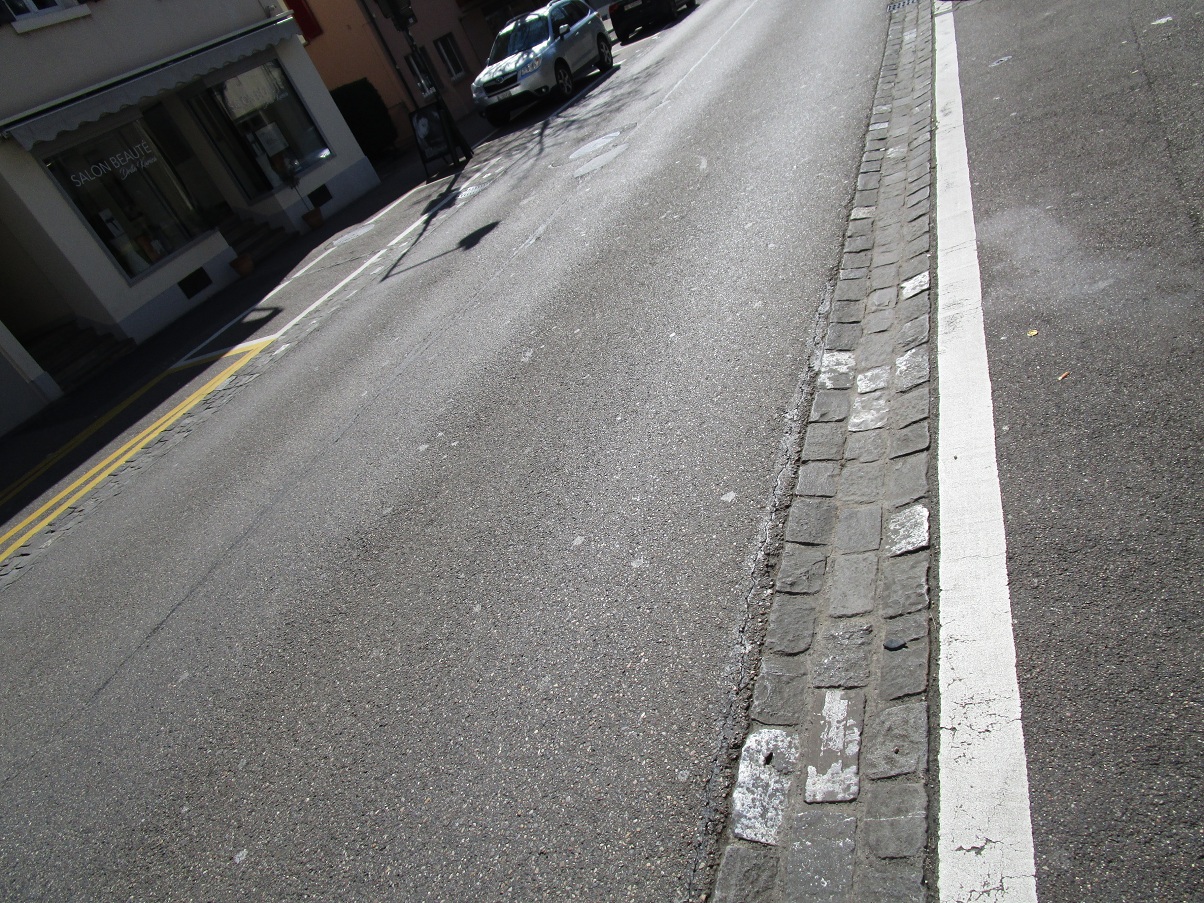 Aesch (Kanton Basel-Land, Schweiz): Trottoir
abgeschafft, Abtrennung durch eine 3zeilige Rinne mit
Pflastersteinen PLUS Sicherheitslinie Aesch
(Kanton Basel-Land, Schweiz): Trottoir abgeschafft,
Abtrennung durch eine 3zeilige Rinne mit
Pflastersteinen PLUS Sicherheitslinie